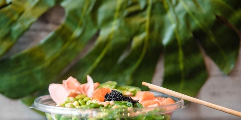 A bowl of poke with chopsticks and sauces next to it