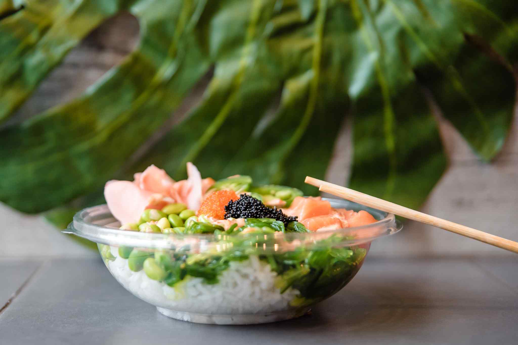 A bowl of poke with chopsticks and sauces next to it